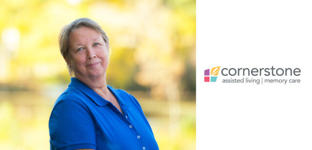 Colleen, the long-serving housekeeping supervisor at Cornerstone Assisted Living, smiles warmly while wearing a blue shirt, set against a soft, natural background.