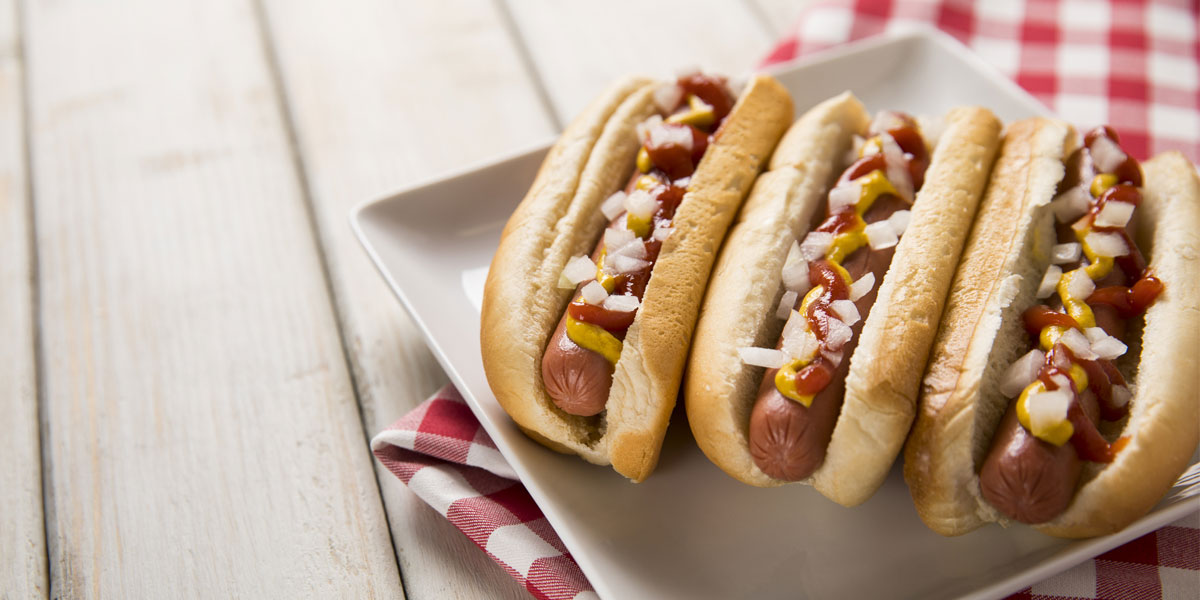 Three hotdogs on buns are featured on a picnic table, similar to the Cornerstone Assisted Living event.