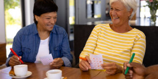 Two women smile and laugh playing bingo, like the event that will take place at Cornerstone Assisted Living.