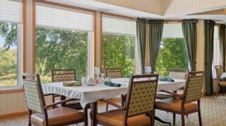 Dining room with table seating and large windows overlooking trees at Cornerstone Assisted Living in Plymouth MN.