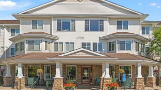 Front exterior entrance with covered porch, seating, and landscaping at Cornerstone Assisted Living in Plymouth MN.