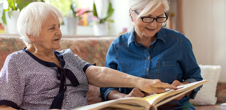 Resident looks at a book with support from a caregiver during a one-on-one activity at a community like Cornerstone Memory Care in Plymouth MN.
