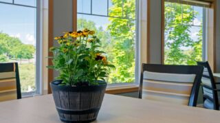 Table with potted flowers and window views in a sunroom at Cornerstone Assisted Living in Plymouth MN.